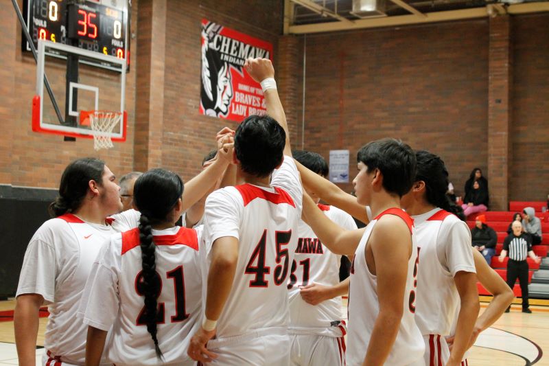 A group of young men in red and white uniforms huddles together in school gym, showing teamwork and camaraderie.