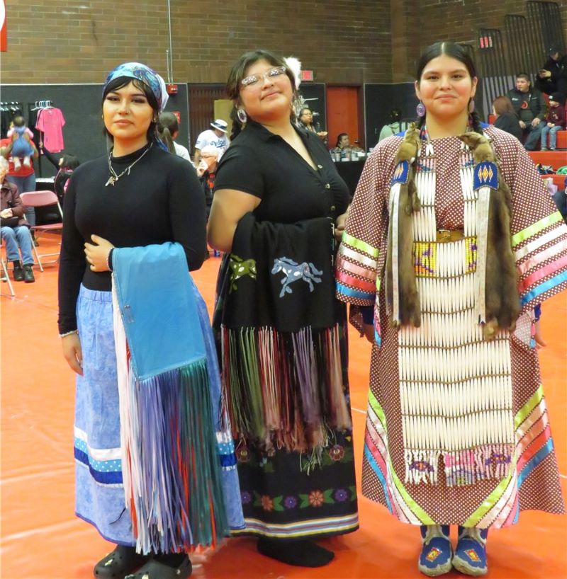 Three female students wearing vibrant native clothing stand side by side, proudly displaying their cultural heritage.