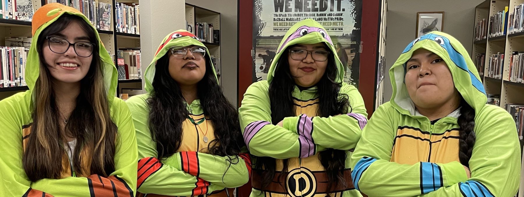 Four students in ninja turtle onsies standing together in the school library.