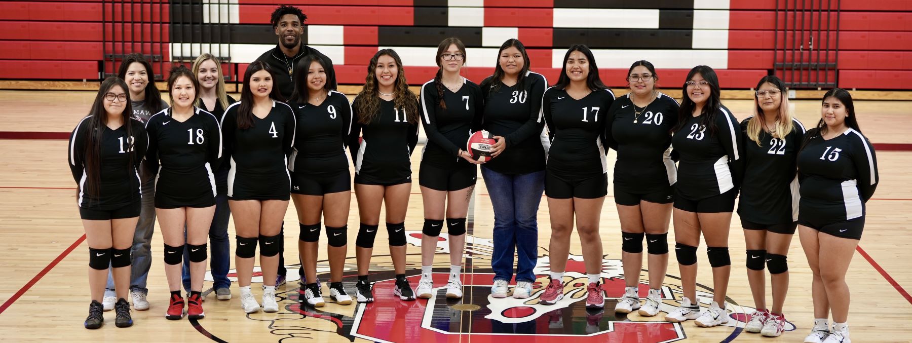 Volleyball team and coach standing together in gym.