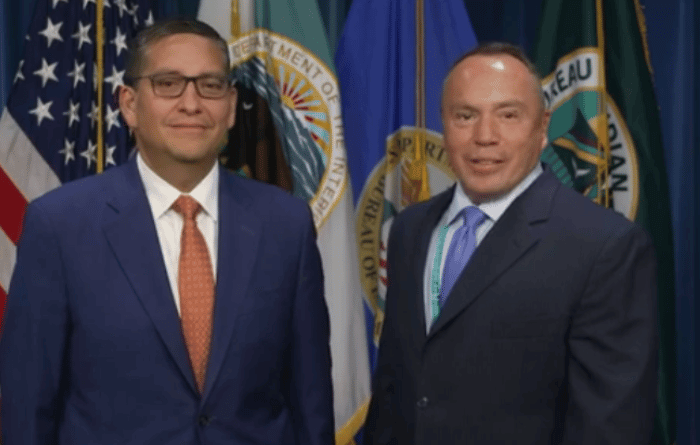 Billy Kirkland and Director Dearman stand side by side in front of U.S. government and BIE flags.