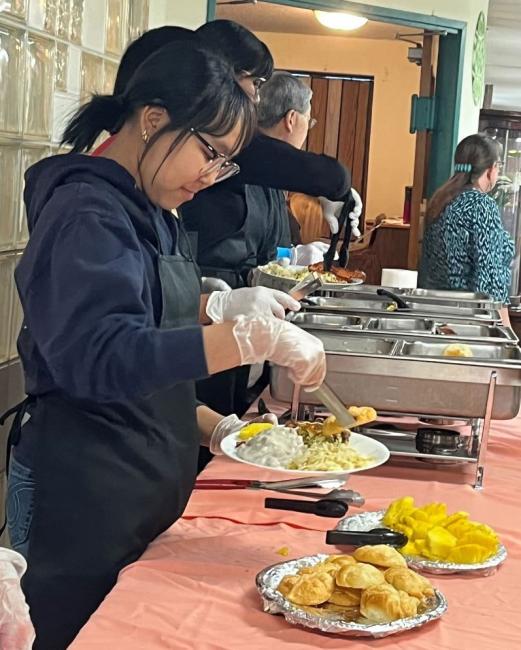 Several individuals are serving delicious food at a buffet table, creating a lively and inviting dining atmosphere.