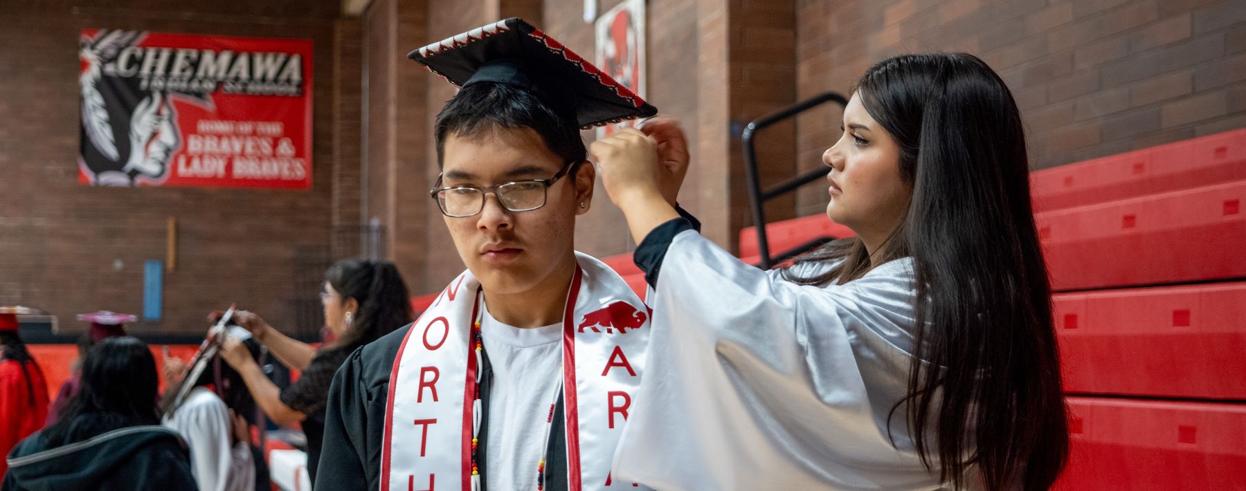 Students receiving help to adjust their graduation caps, celebrating their achievement at school.