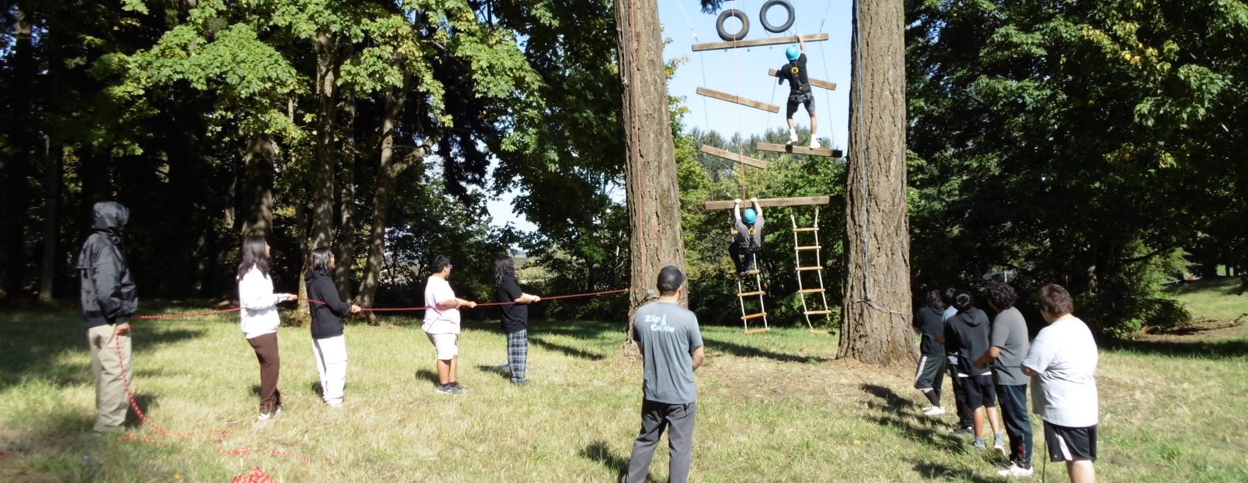 Students stand outside, excited to climb ladders and face outdoor challenges at their school.