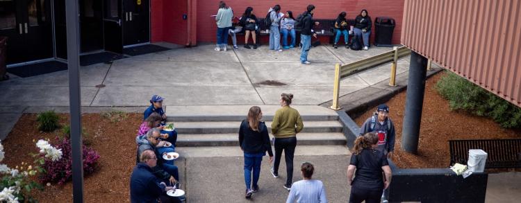 Several people gathered outside a school, smiling and talking as they wait for classes to start.